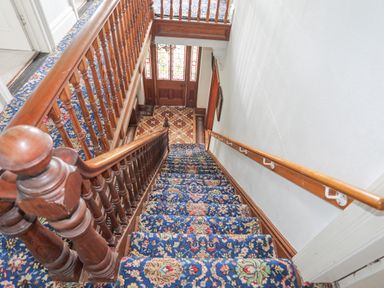 A stairway with floral patterned carpet and wooden banisters leading to a door with stained glass panels at Llys Owen in Criccieth