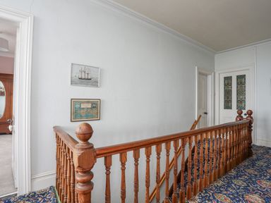 A hallway with wooden banister stairs and framed pictures on the wall at Llys Owen in Criccieth