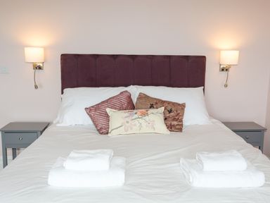 A bedroom with a double bed with white sheets and pillows and folded towels on top at Llys Owen in Criccieth