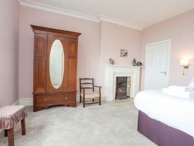 A bedroom with a wooden wardrobe with a mirror a chair a fireplace and a bed at Llys Owen in Criccieth
