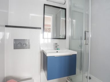 A bathroom with a blue vanity sink cabinet a wall-mounted mirror a glass shower enclosure and a built-in toilet cistern at Llys Owen in Criccieth