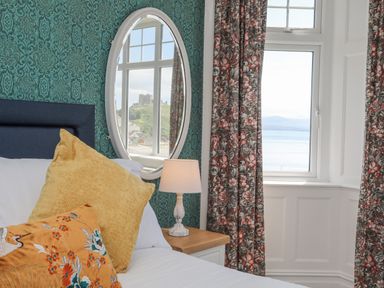 A bedroom with a bed with yellow and patterned pillows a bedside lamp and floral curtains at Llys Owen in Criccieth