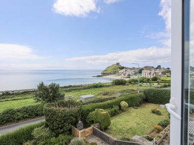 A view of a coastal town with a hilltop castle sea green fields and a garden from a window at Llys Owen in Criccieth