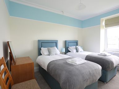 A bedroom with two single beds with pillows and blankets a wooden desk with a mirror and a chair near a window at Llys Owen in Criccieth