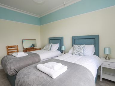 A bedroom with two single beds with grey throws and white towels on them at Llys Owen in Criccieth