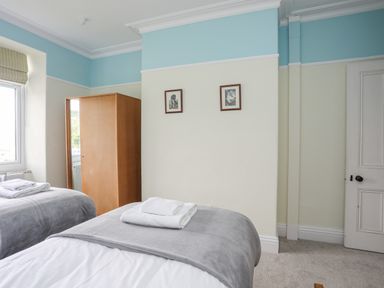 A bedroom with two single beds a wooden wardrobe and two framed pictures on the wall at Llys Owen in Criccieth