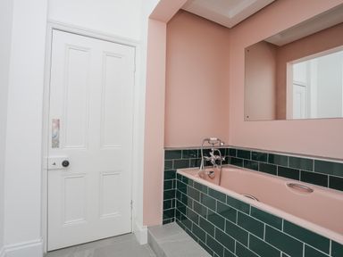 A bathroom with a pink bathtub surrounded by dark green tiles and a white door at Llys Owen in Criccieth