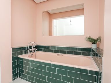 A bathroom with a bathtub surrounded by green tiles and a large mirror on a pink wall at Llys Owen in Criccieth