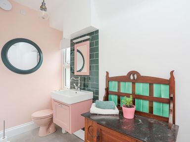 A bathroom with a pink toilet and sink a round mirror and a wooden bench with a plant and towels at Llys Owen in Criccieth