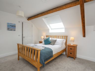 A bedroom with a wooden bed frame bedside tables and exposed wooden beams at Llys Owen in Criccieth