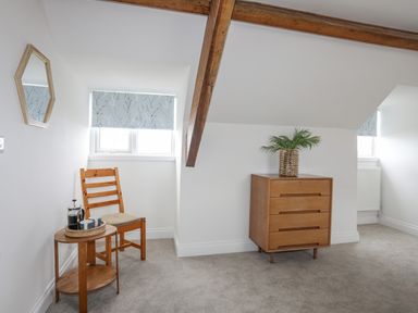 A room with carpeted floor wooden chair and table with cups and a wooden chest of drawers with a plant at Llys Owen in Criccieth