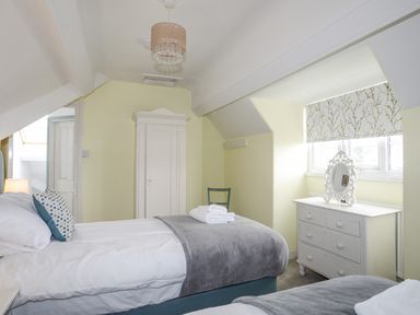 A bedroom with two single beds a white wardrobe a dresser with a mirror and a window with patterned blind at Llys Owen in Criccieth