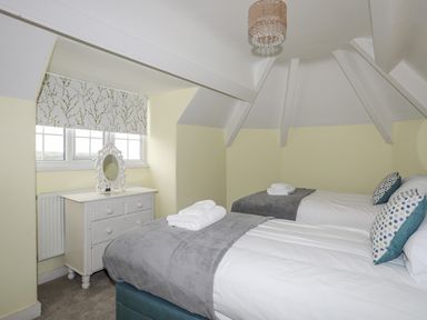 A bedroom with two single beds with gray blankets and pillows beside a window with floral curtain at Llys Owen in Criccieth