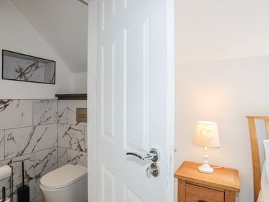 A bathroom with a white toilet and marble tiles partially visible behind a white door next to a wooden bedside table with a lamp at Llys Owen in Criccieth