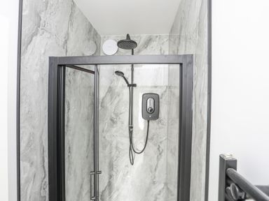 A shower with a black frame and marble patterned walls at Llys Owen in Criccieth