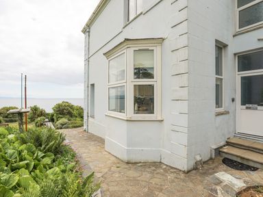 Exterior corner view of a white house with a bay window and garden path at Llys Owen in Criccieth