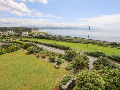 A coastal view with green fields a road bushes and parked cars near the sea at Llys Owen in Criccieth