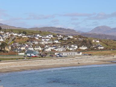 A coastal view with a beach houses on a hillside and mountains in the background at Llys Owen in Criccieth