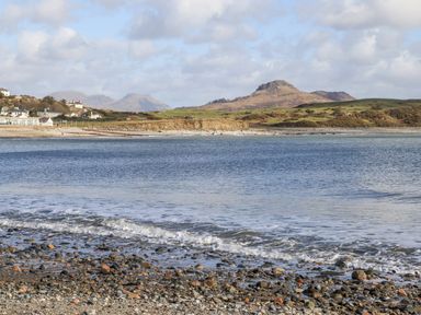 A rocky beach with waves and hills in the background at Llys Owen in Criccieth