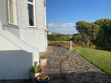 A stone pathway beside a house with potted plants and bushes and a lawn at Llys Owen in Criccieth