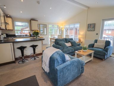 An open living room and kitchen with three blue armchairs a wooden coffee table two black bar stools and a dining table at Hill Top Lodge in Bowness 65 White Cross Bay