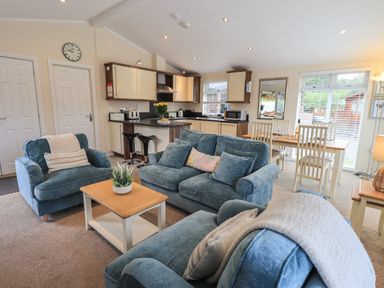 A living area with blue sofas a coffee table and an open kitchen with dining table at Hill Top Lodge Bowness 65 White Cross Bay