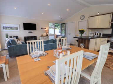 A dining table set with plates and glasses next to a living room with blue sofas and a kitchen with cream cabinets at Hill Top Lodge in Bowness 65 White Cross Bay