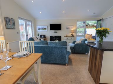 A living room with blue sofas a dining table with glasses and plates and a countertop with flowers at Hill Top Lodge in Bowness 65 White Cross Bay