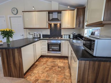 A kitchen with cream cabinets wood accents a black countertop a stove oven microwave sink and flowers on the counter at Hill Top Lodge in Bowness 65 White Cross Bay