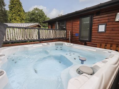 An outdoor hot tub with water and jets next to a wooden cabin with rope railing at Hill Top Lodge in Bowness 65 White Cross Bay