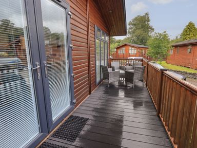 A wooden balcony with a table and chairs outside a cabin at Hill Top Lodge in Bowness 65 White Cross Bay