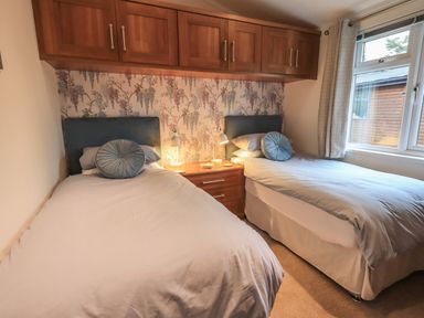 A bedroom with two single beds a wooden cabinet above a bedside table and a window at Hill Top Lodge in Bowness 65 White Cross Bay