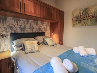 A bedroom with a double bed with pillows and towels wooden cabinets and floral wallpaper at Hill Top Lodge in Bowness 65 White Cross Bay
