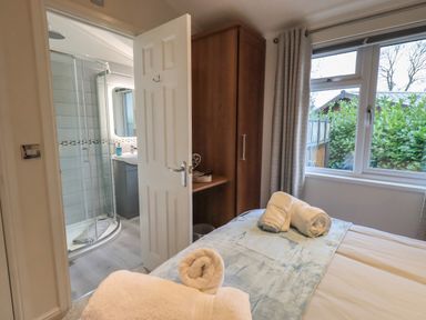 A bedroom with a bed covered with towels next to a wooden wardrobe and an open door leading to a bathroom with a shower at Hill Top Lodge in Bowness 65 White Cross Bay
