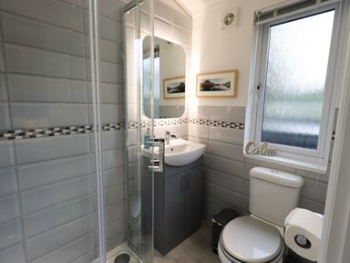 A bathroom with a shower enclosure a sink with cabinet a toilet and a window with a calm decoration at Hill Top Lodge in Bowness 65 White Cross Bay
