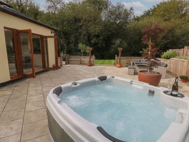 An outdoor patio with a hot tub glass doors and a seating area at Rudbaxton Water in Rudbaxton near Haverfordwest