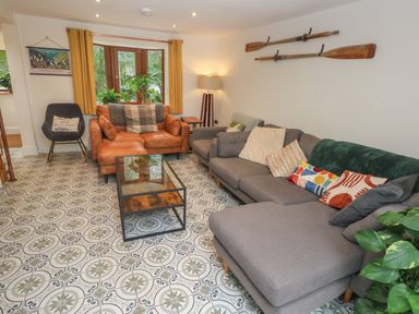 A living room with a gray sectional sofa and a brown leather loveseat near windows with plants at Rudbaxton Water Rudbaxton near Haverfordwest