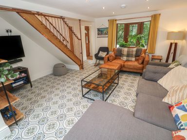 A living room with patterned floor tiles a staircase a glass coffee table a gray sofa and a brown leather armchair with yellow curtains at Rudbaxton Water Rudbaxton near Haverfordwest