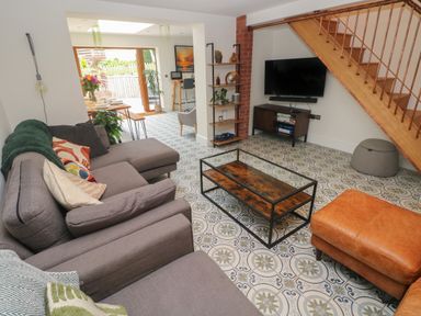 A living room with a gray sectional sofa a glass coffee table a TV under wooden stairs and a dining area in the background at Rudbaxton Water Rudbaxton near Haverfordwest
