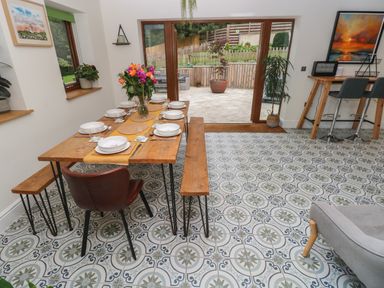 A dining area with a wooden table set for six people with benches and chairs a vase of flowers on the table patterned tiled floor and large glass doors opening to a patio at Rudbaxton Water Rudbaxton near Haverfordwest
