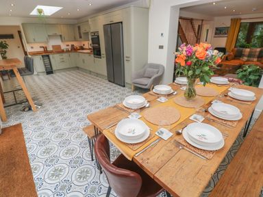 A kitchen and dining area with a wooden dining table set with bowls and glasses and green cabinetry in the kitchen at Rudbaxton Water in Rudbaxton near Haverfordwest