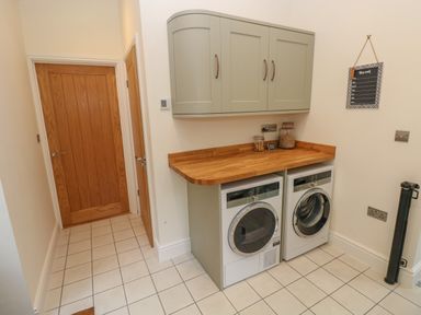 A laundry room with two front-loading washing machines under a wooden countertop and green wall cabinets at Rudbaxton Water in Rudbaxton near Haverfordwest