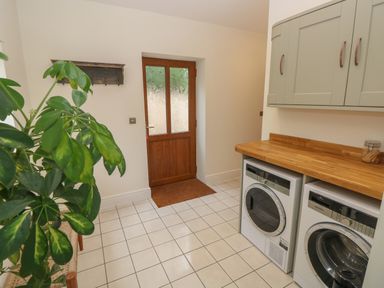 A utility room with a wooden door a plant on the left two appliances under a wooden countertop and wall cabinets at Rudbaxton Water Rudbaxton near Haverfordwest