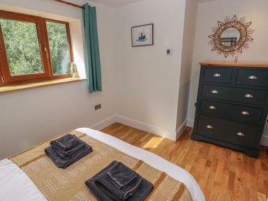 A bedroom with a bed with folded towels a window with green curtains a chest of drawers and a decorative mirror at Rudbaxton Water Rudbaxton near Haverfordwest