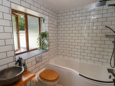 A bathroom with a bathtub, a toilet with a wooden seat, a stone sink on a wooden countertop, and a window with a hanging plant at Rudbaxton Water Rudbaxton near Haverfordwest