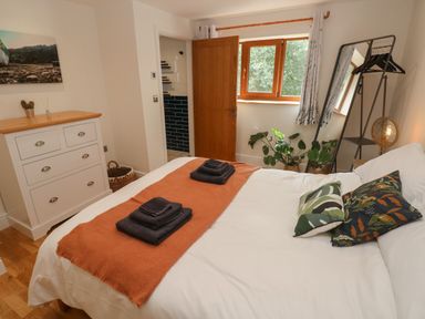 A bedroom with a bed with pillows and folded towels a dresser a window a standing mirror with hangers and plants at Rudbaxton Water Rudbaxton near Haverfordwest