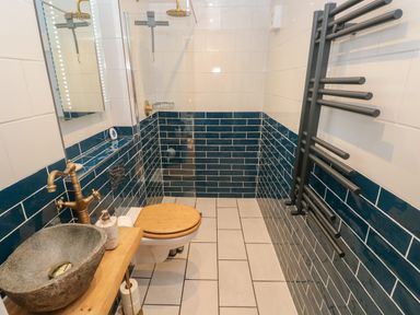 A bathroom with a stone basin sink wooden toilet seat and a shower area with blue and white tiled walls at Rudbaxton Water in Rudbaxton near Haverfordwest