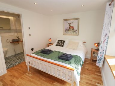 A bedroom with a white bed and green blanket towels on it bedside tables with lamps a framed deer picture on the wall and an open door to a bathroom at Rudbaxton Water in Rudbaxton near Haverfordwest