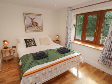A bedroom with a bed with pillows and folded towels by a window with curtains and bedside tables with lamps at Rudbaxton Water in Rudbaxton near Haverfordwest