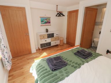 A bedroom with a bed covered by a green throw and folded towels a wooden dresser with a plant a wooden floor and three wooden doors at Rudbaxton Water Rudbaxton near Haverfordwest